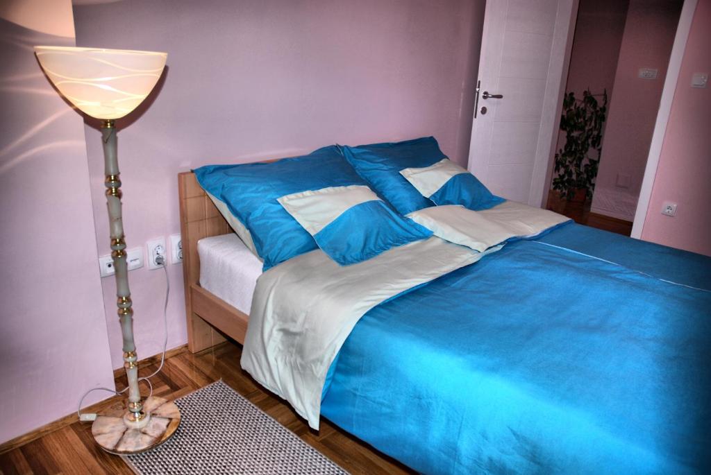 a bedroom with a bed with blue sheets and a lamp at Apartman Milkovic 2 in Sombor