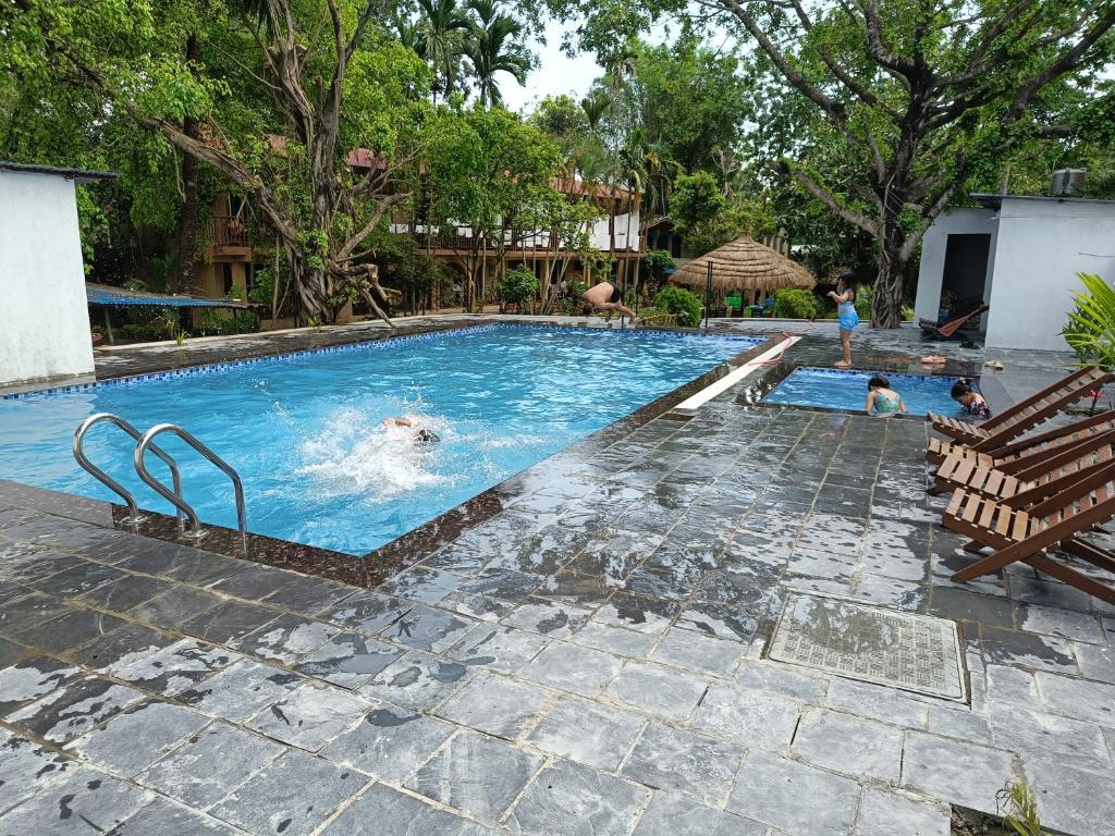 a swimming pool with people in the water at Chitwan Tiger Camp in Sauraha