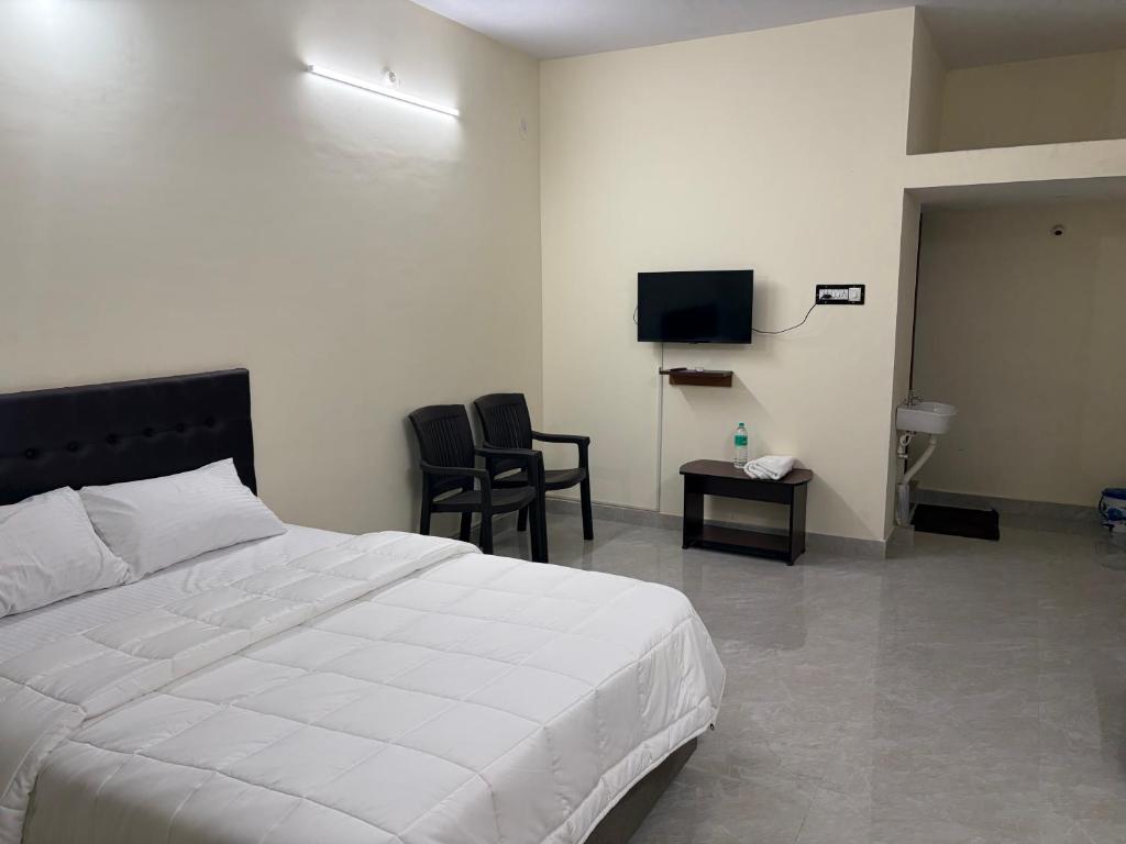 a bedroom with a bed and two chairs and a television at Balaas Inn in Karaikal