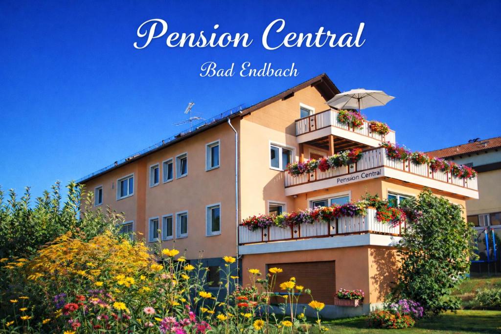 a building with a balcony with flowers and an umbrella at Pension Central Ferienwohnungen in Bad Endbach