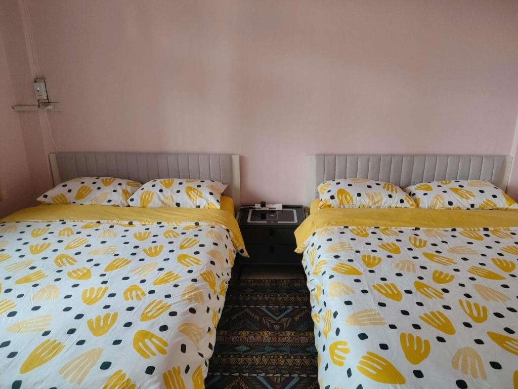 two beds in a small bedroom with yellow and white sheets at REHome in Bangkok