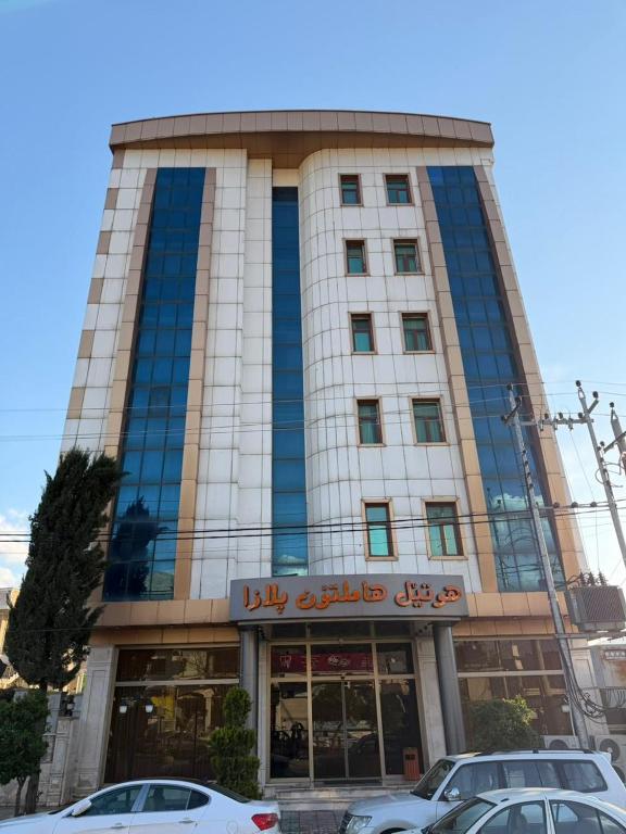 a building with cars parked in front of it at Hamilton Plaza Hotel in Diyānah