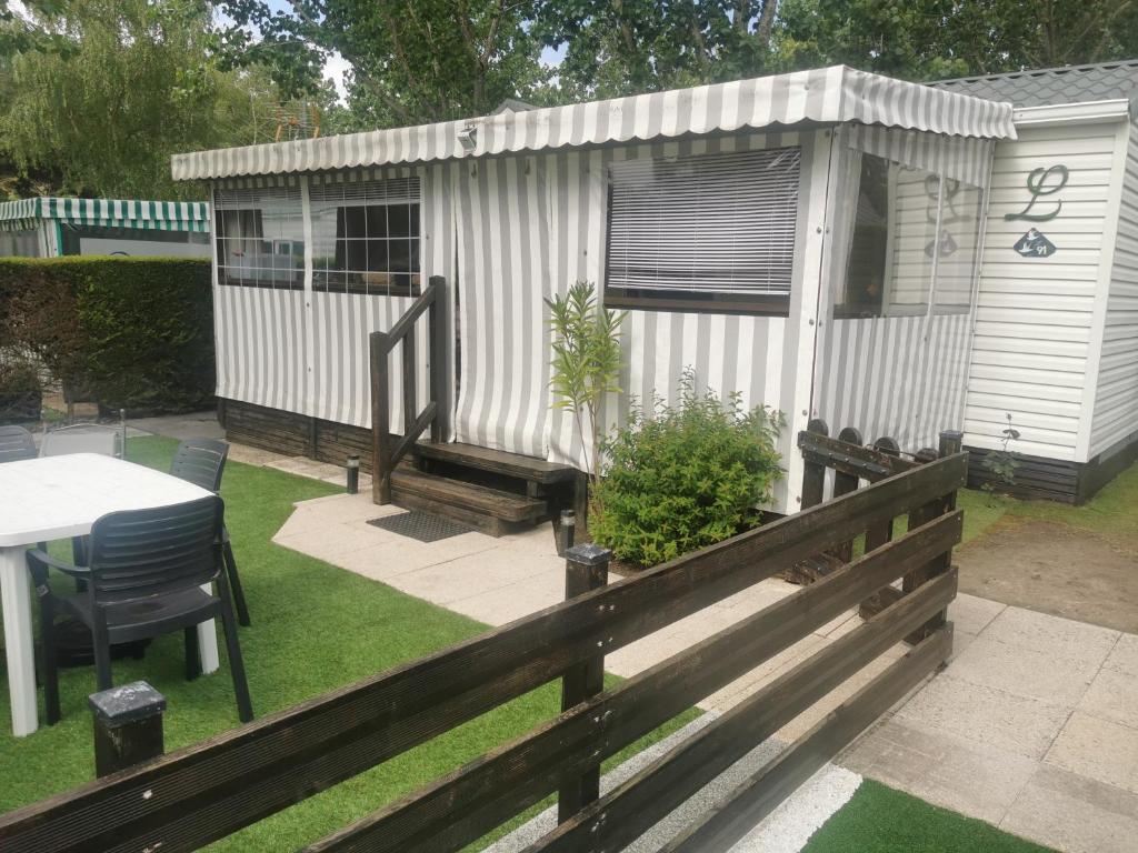 a small white shed with a table and a fence at Mobil-home cosy avec terrasse et jardin privatif in La Bernerie-en-Retz