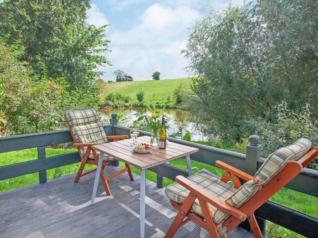 a table and chairs on a deck with a view of a river at Coot Roundhouse - Uk33890 in Cullompton