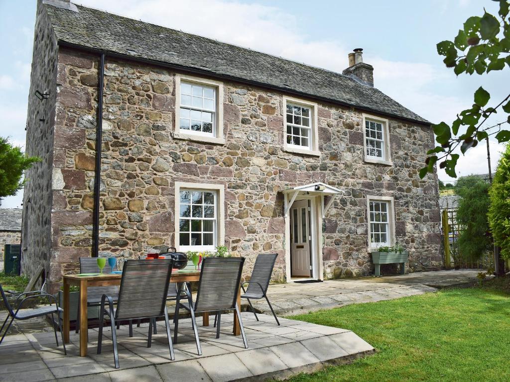 a table and chairs in front of a stone house at Waterloo Farm House in Bankfoot