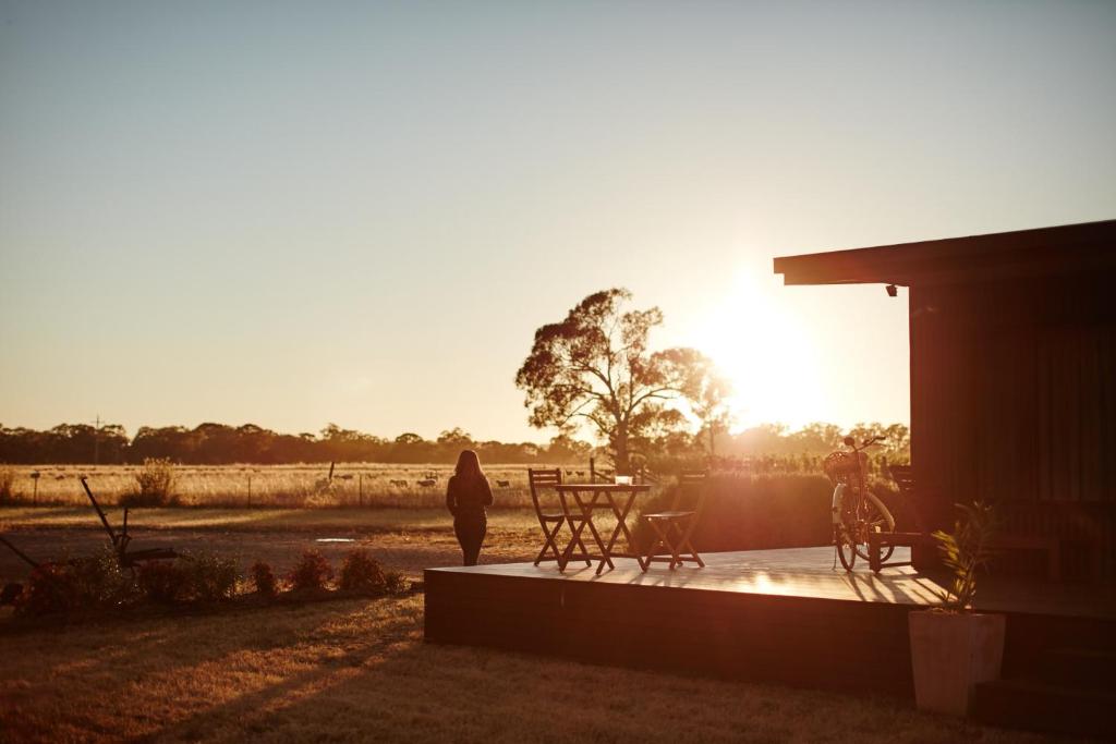 a woman standing on the porch of a house with the sunset at Moodemere Lake House in Rutherglen