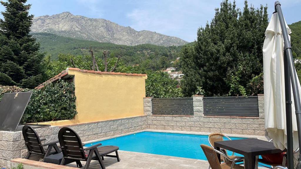 a swimming pool with chairs and a table and an umbrella at Casa La Rubía de Gredos in Cuevas del Valle