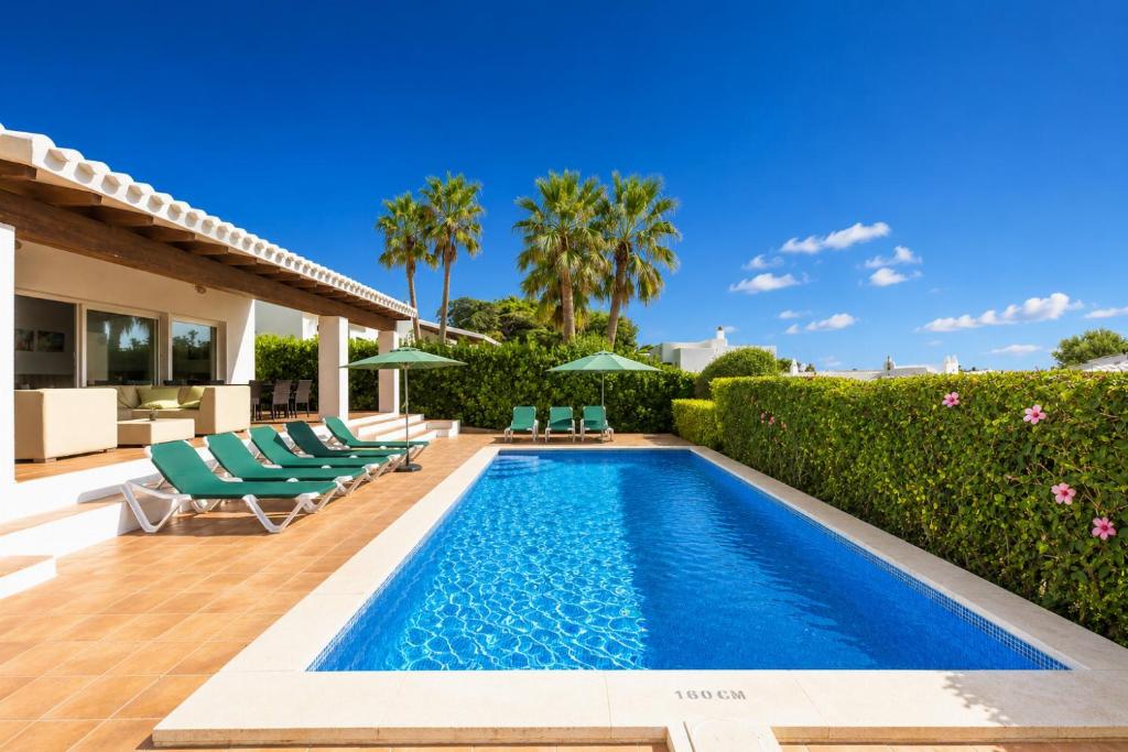a swimming pool in a backyard with lounge chairs and a villa at Villa Binipaco in Binibeca