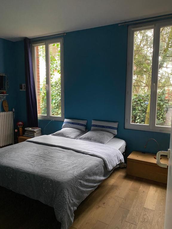 a bedroom with a bed with blue walls and windows at Chambre chez l'habitant dans grande maison Arborée in Orly