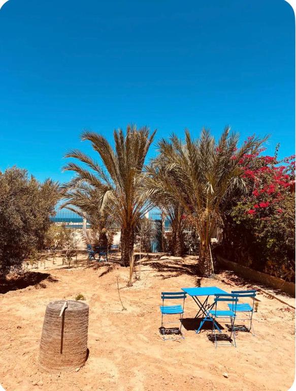 two chairs and a table on a beach with palm trees at Résidence 3 M in Jāmi‘ al Guelloufi