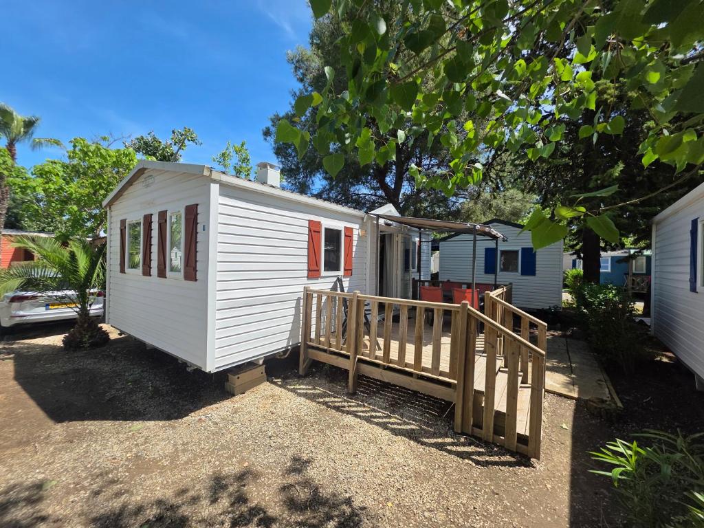 a small white tiny house with a wooden porch at Vias Plage - Camping Les Salisses - Mobilhome in Vias