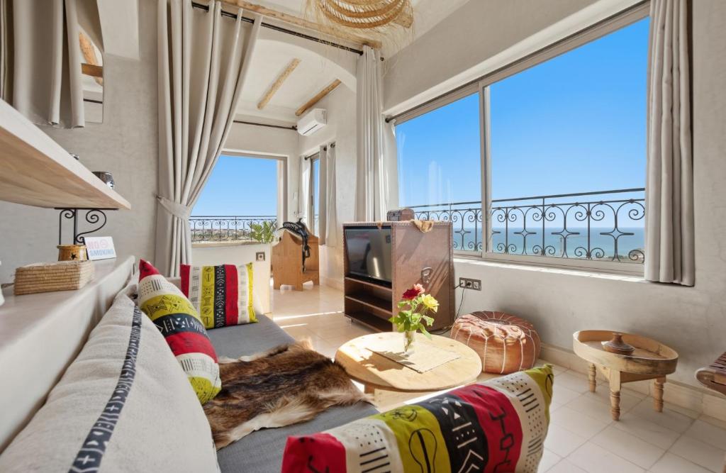 a living room with a couch and a tv and windows at Surf Appart Morocco in Tamraght Ouzdar