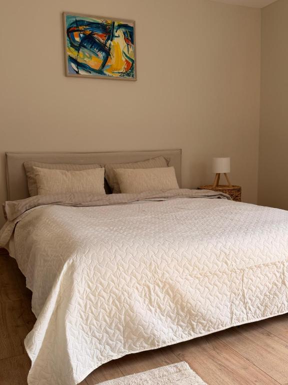 a bedroom with a white bed with a painting on the wall at Sunset holiday house in Liepāja
