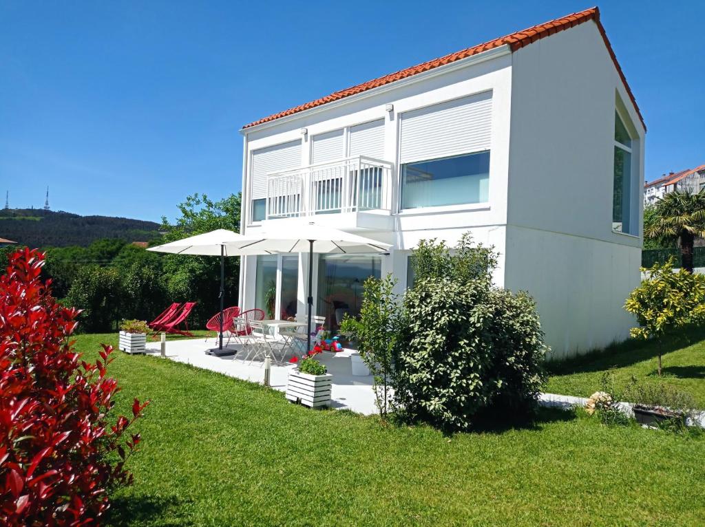 a white house with an umbrella and a yard at LAR JARDÍN - Casas independientes con jardín y parking privado in Santiago de Compostela