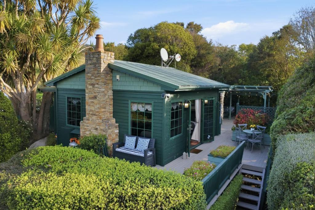 a green shed with a brick chimney and a patio at Private seaside couples hideaway in Kaka Point