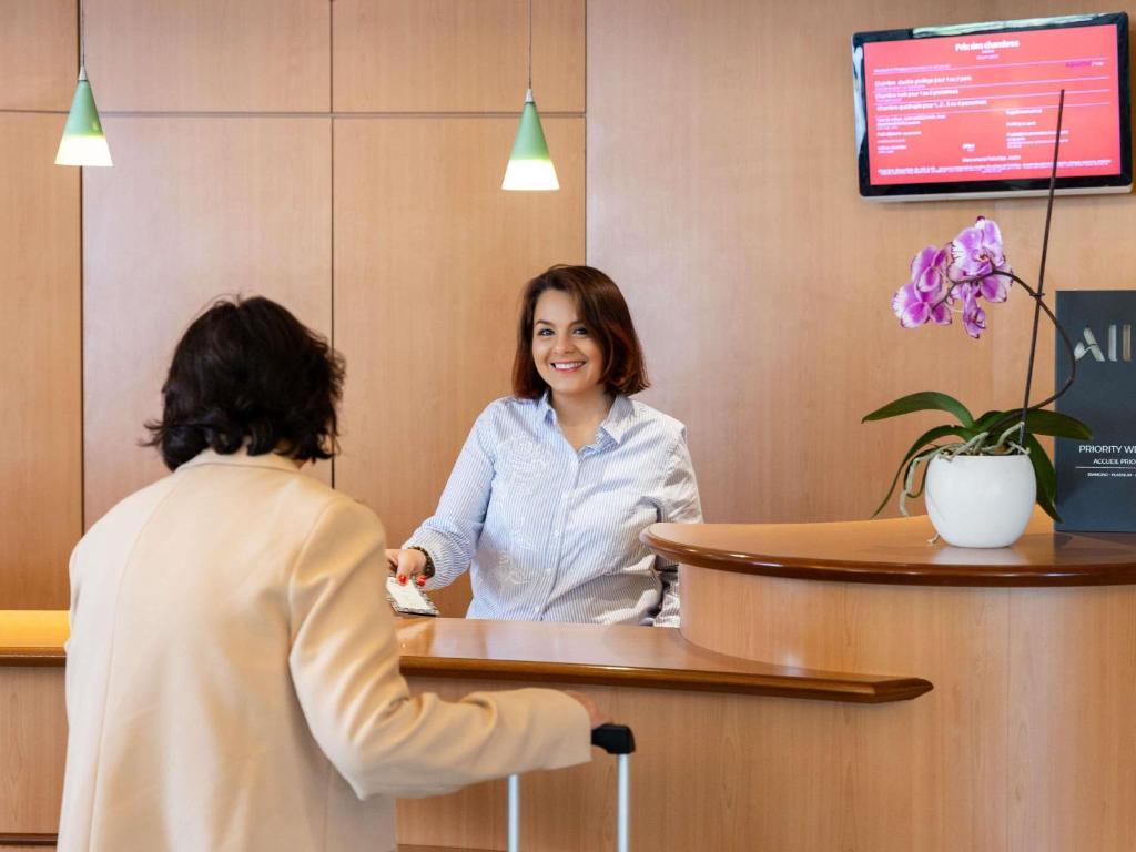 a woman standing at a reception desk in a waiting room at ibis Auch in Auch