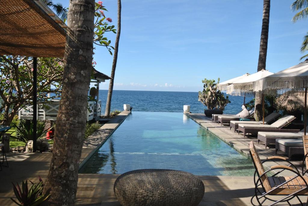 a swimming pool with chairs and the ocean in the background at Villa Pantai Matanai in Tianyar