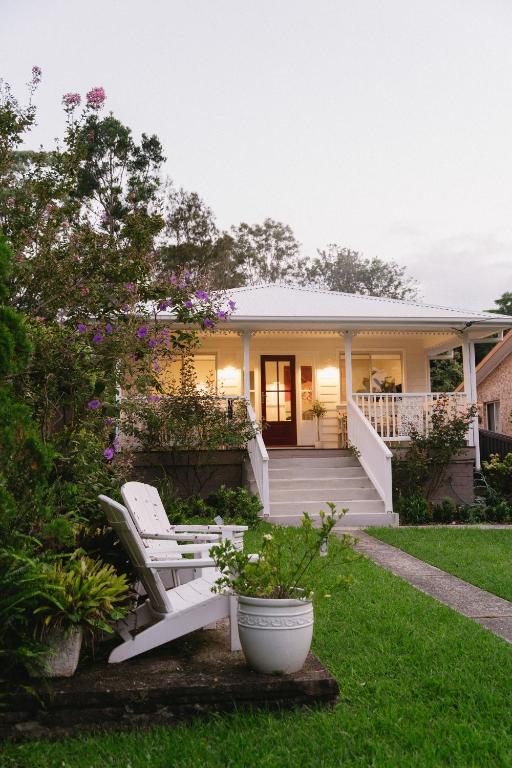 a house with two white chairs in the yard at Lady Rose Cottage Jamberoo in Jamberoo