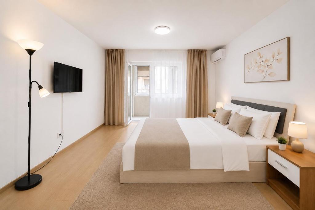 a white bedroom with a large bed and a television at Nicolle Elite Apartment in Piteşti