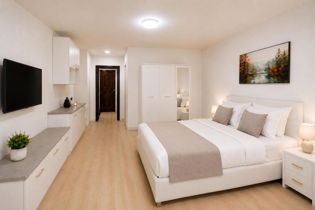 a white bedroom with a large bed and a flat screen tv at Nicolle Prestige Apartment in Piteşti