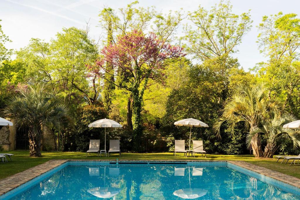 a swimming pool with two umbrellas and trees at Hôtel - Restaurant & Spa La Magdeleine - Mathias Dandine in Gémenos