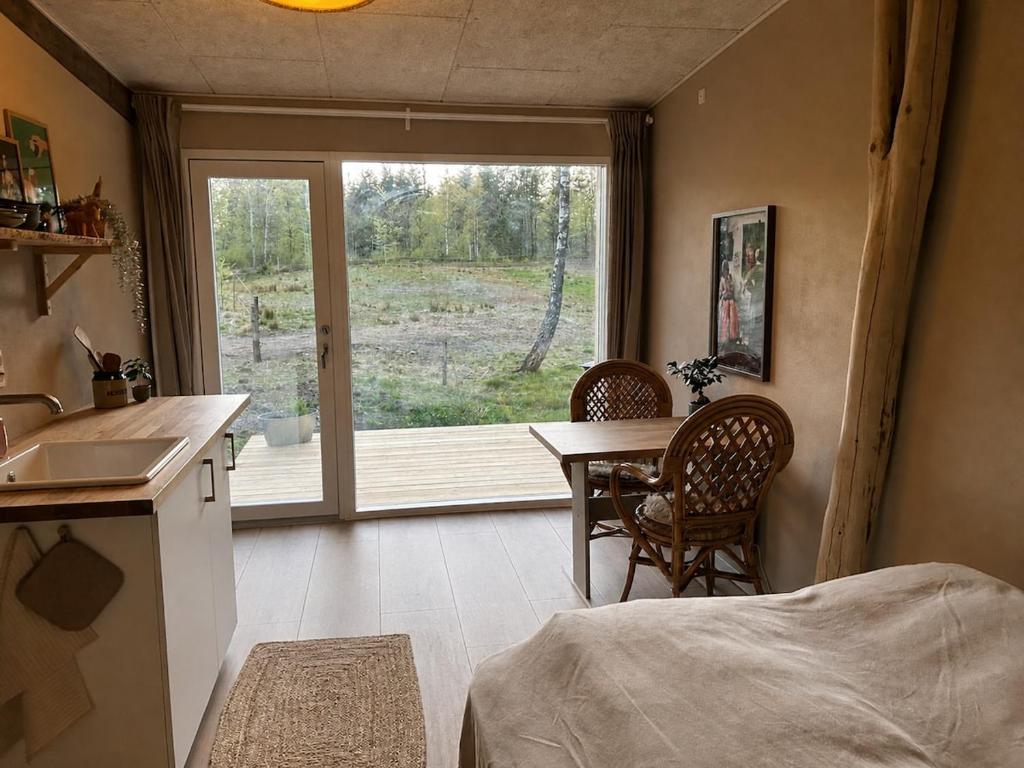 a bedroom with a table and a kitchen with a window at Hulen - Ro & Natur in Bindslev