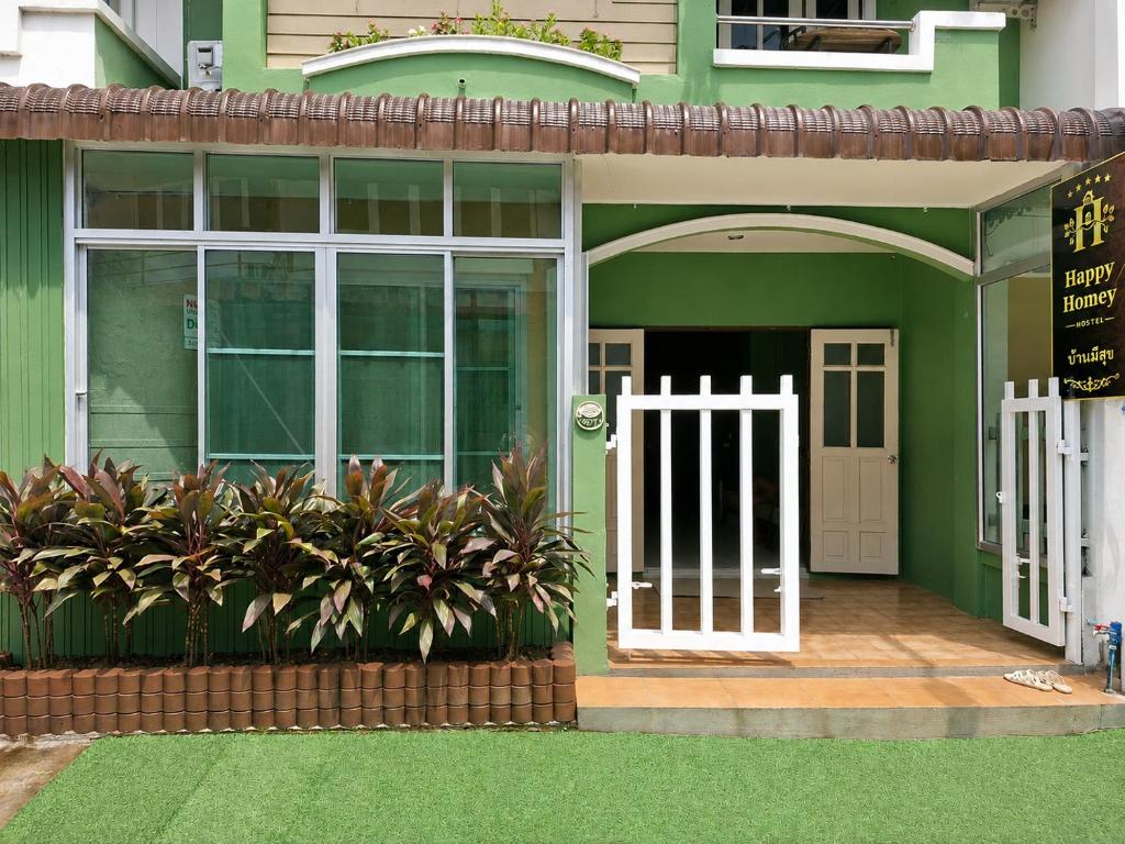 a green house with a white door and some plants at Happy Homey Hostel in Suratthani