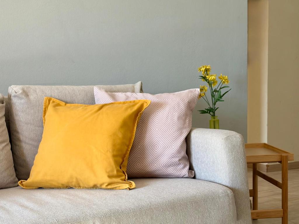 a couch with a yellow pillow and a vase of flowers at Delta Apartment • next to the beach in Roda