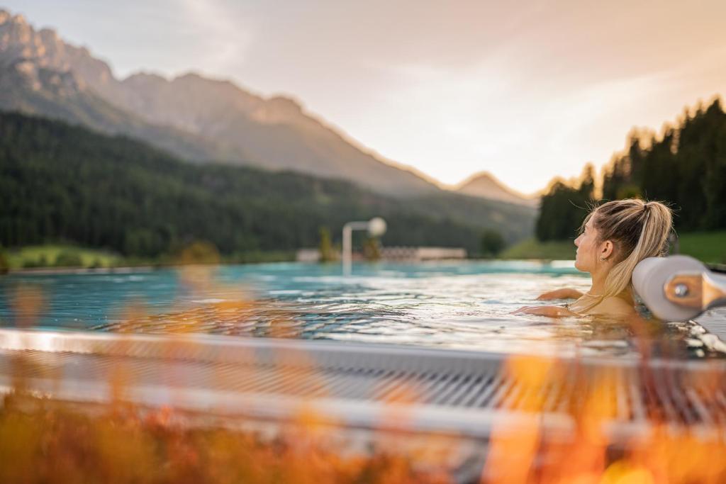 a woman in a swimming pool with mountains in the background at Loewe Dolomites in San Candido