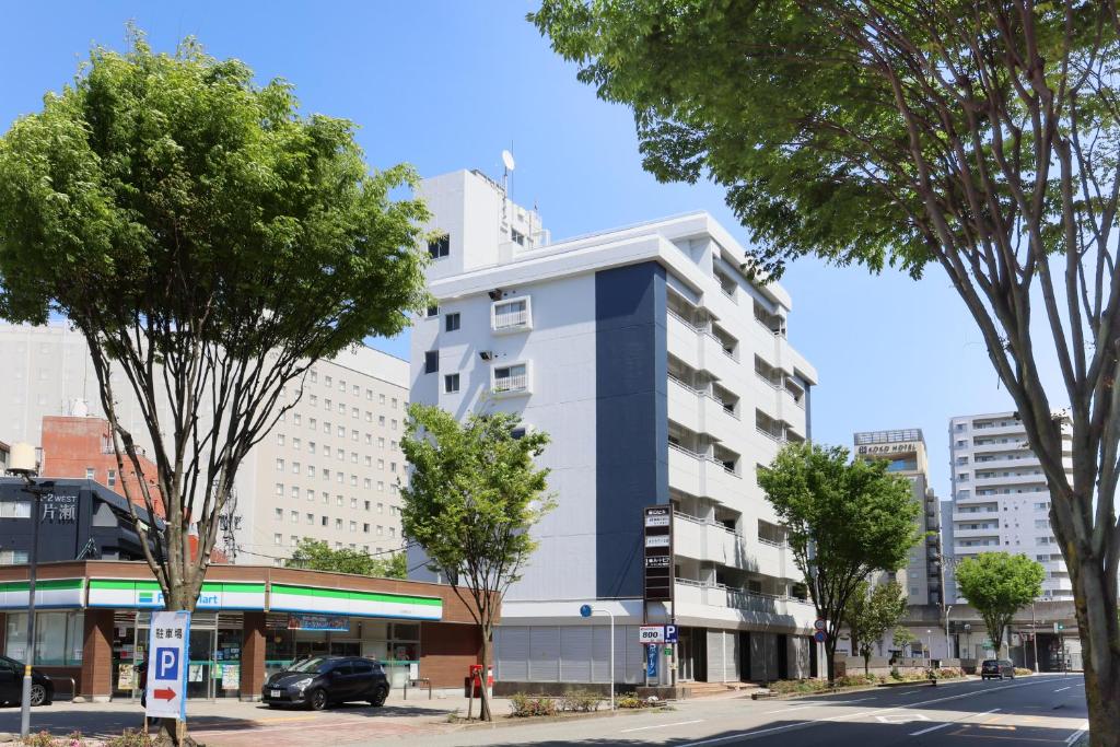 a tall white building on a city street with trees at Desroches House in Kanazawa