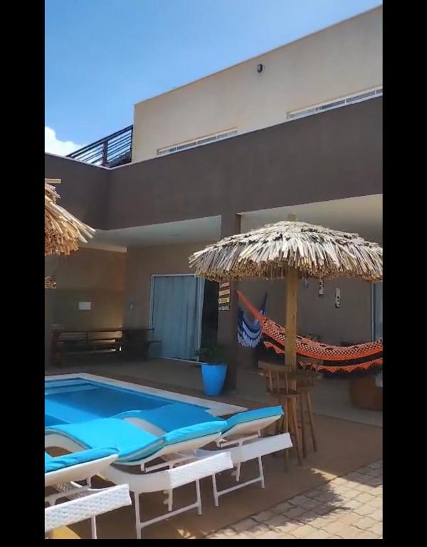 a house with a swimming pool with chairs and an umbrella at Refúgio Tropical in Touros