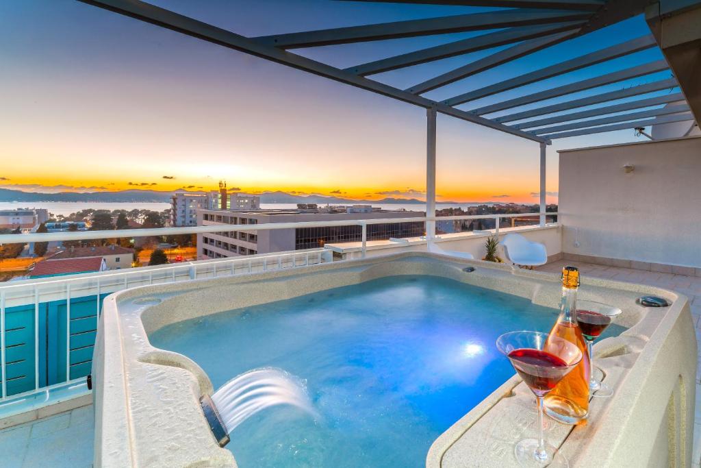 扎達爾的住宿－Sunset Penthouse Apartment with Jacuzzi and Seaview，一座建筑物屋顶上的游泳池,上面有酒杯