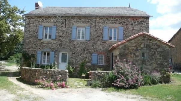 a large stone house with blue windows and flowers at Gîte La Mirgue in Sanvensa
