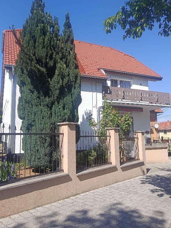 a white house with a fence and a tree at Anna Vendégház in Hévíz