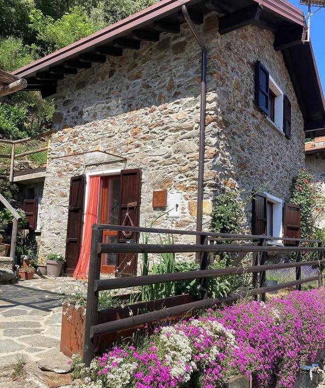 a stone house with flowers in front of it at Baita LoKa-Baita panoramica tra Lago di Como e Grigna in Bellano