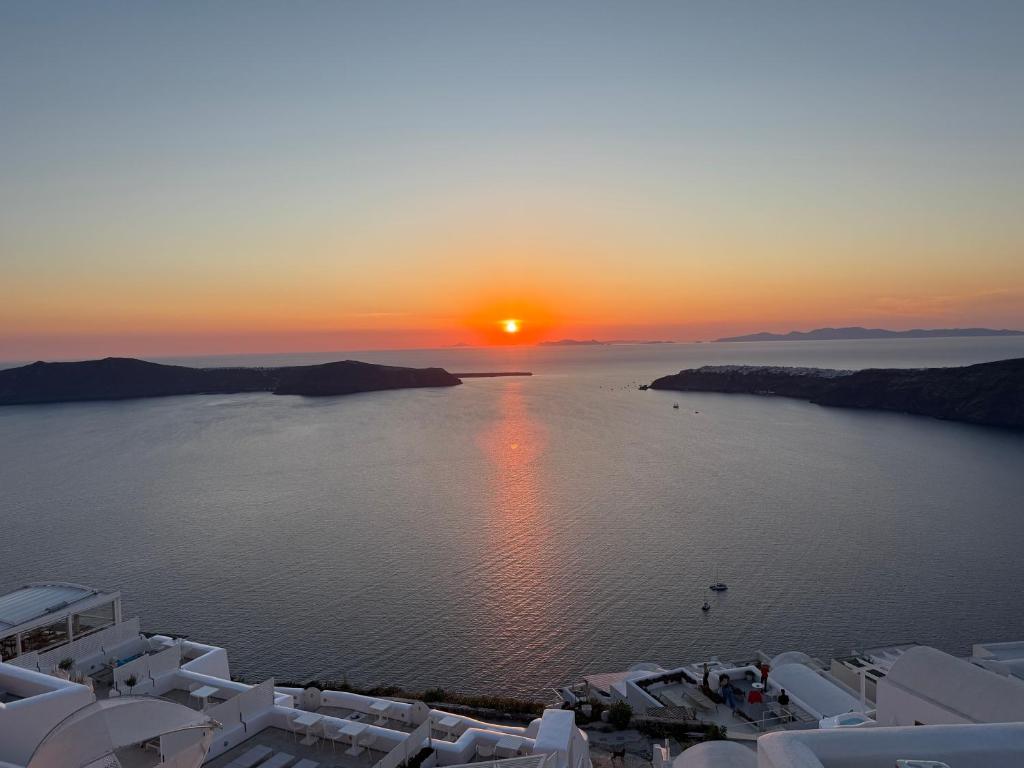 a sunset over a large body of water with white buildings at Esmi Suites Santorini in Imerovigli