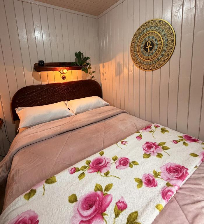 a bed with a blanket with pink flowers on it at Pousada Nó de Pinho - Kitnet Microcasa in São Joaquim