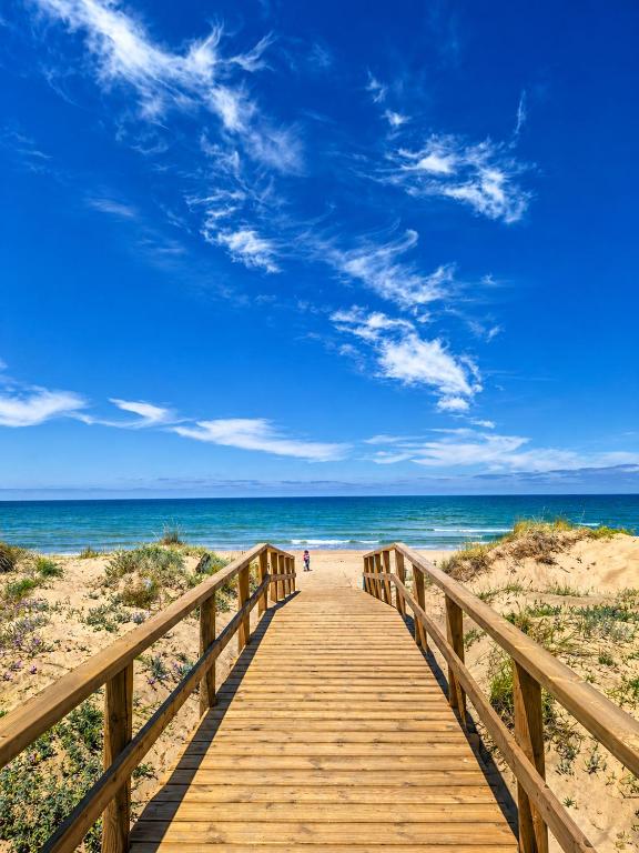 a wooden boardwalk to the beach under a blue sky at Sunrise House Oliva Nova Beach & MET Apartment in Oliva