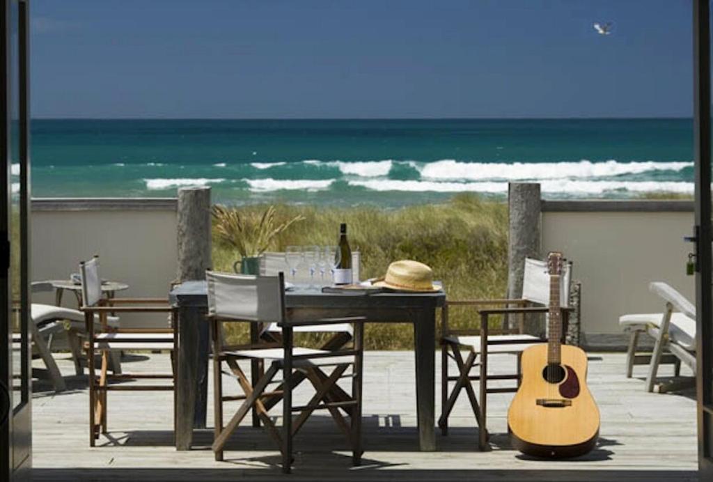 a table and chairs with a guitar on the beach at The Bach - beachfront in Waimarama