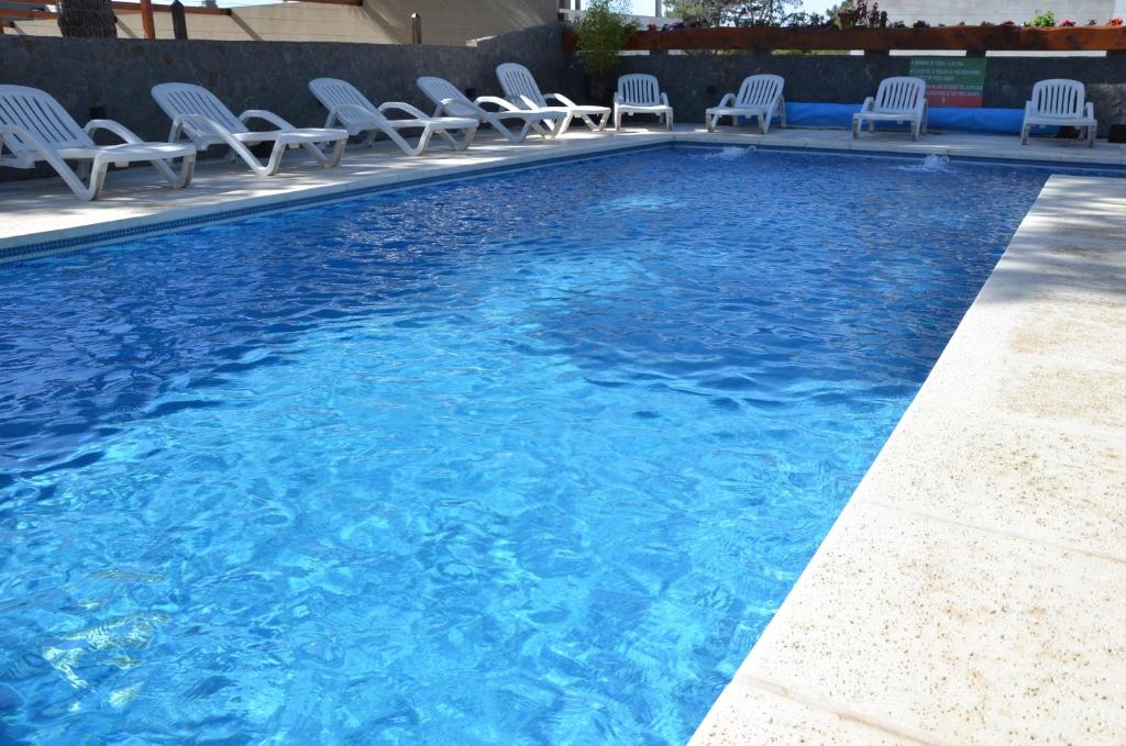 a swimming pool with chairs and blue water at Picun Cuyen in Villa Gesell