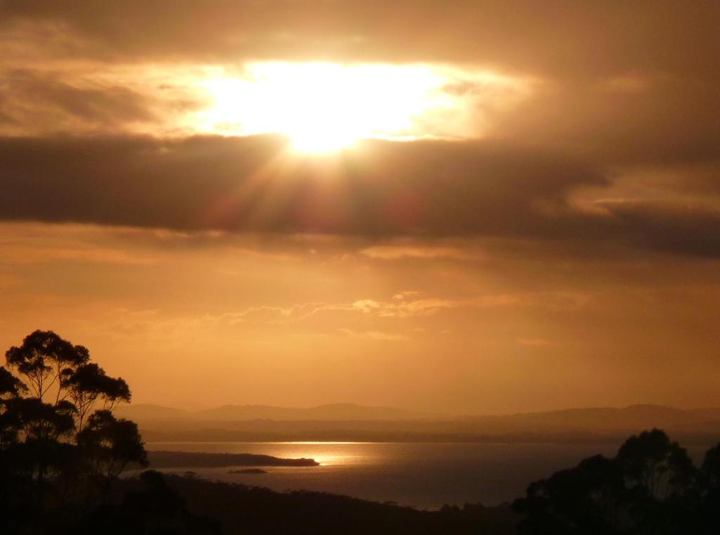 a sunset over the water with the sun in the sky at Innisfree Mountain Retreat in Denmark