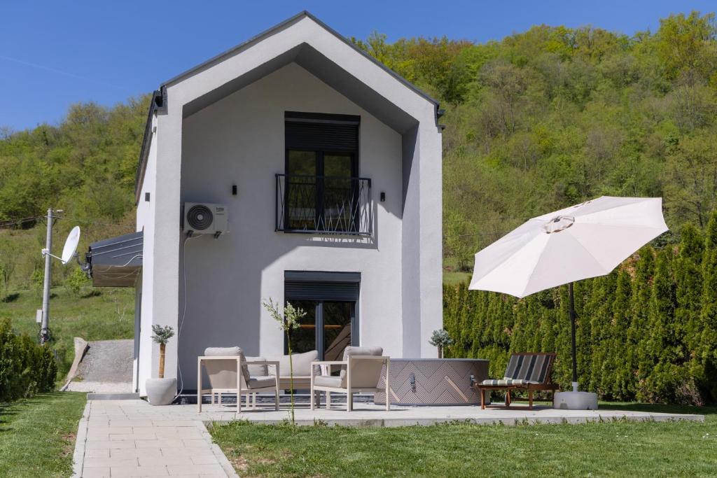 a white house with chairs and an umbrella at Villa Alba Rekavice Krupa na Vrbasu in Banja Luka