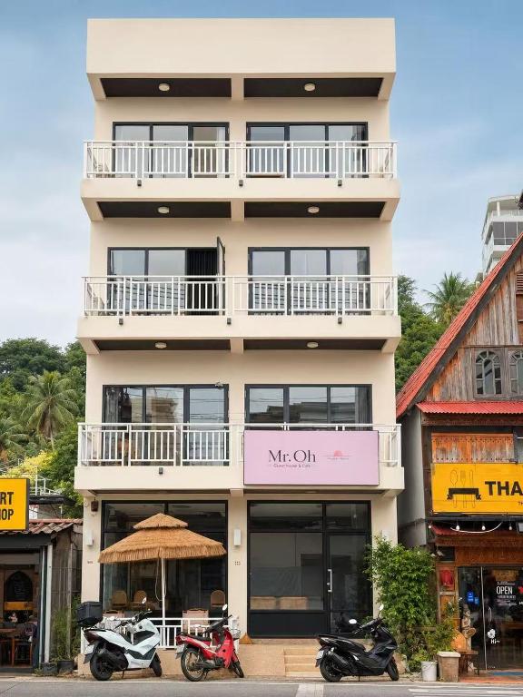 a tall white building with motorcycles parked in front of it at Mr Oh in Phuket Karon in Ka Rorn