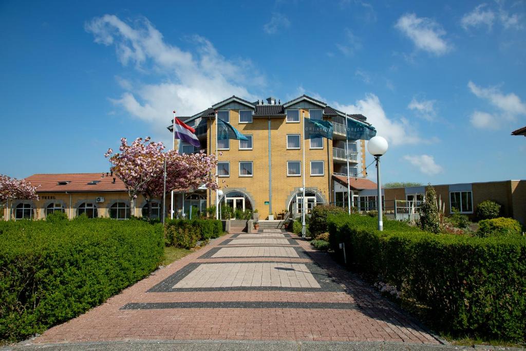a large yellow building with a brick walkway at Hotel Greenside Texel in De Koog