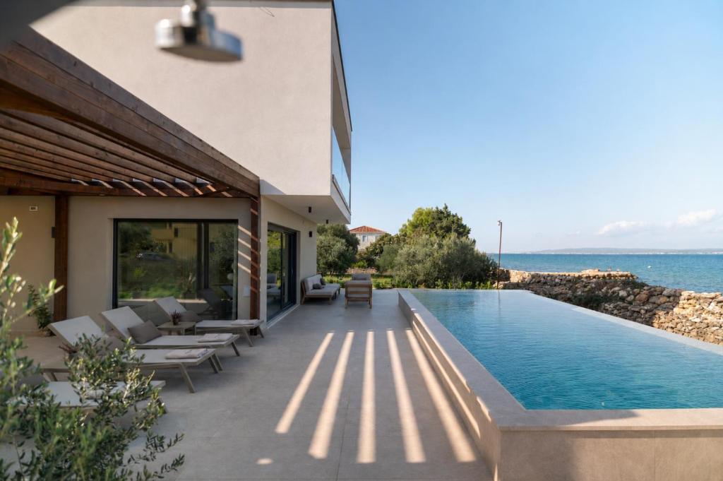 a house with a swimming pool next to the ocean at Courtside Luxury Villa Dalmatia in Dobropoljana