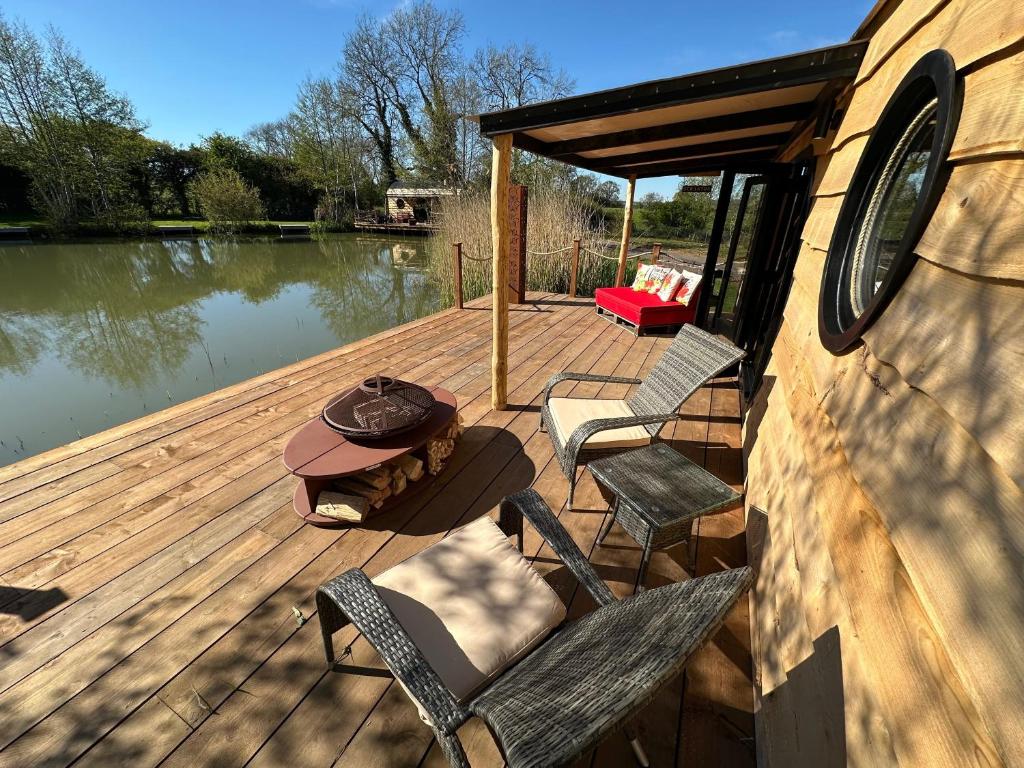 a wooden deck with chairs and a table on a lake at Scranton luxury fishing pod with private fishing Jetty in Spilsby
