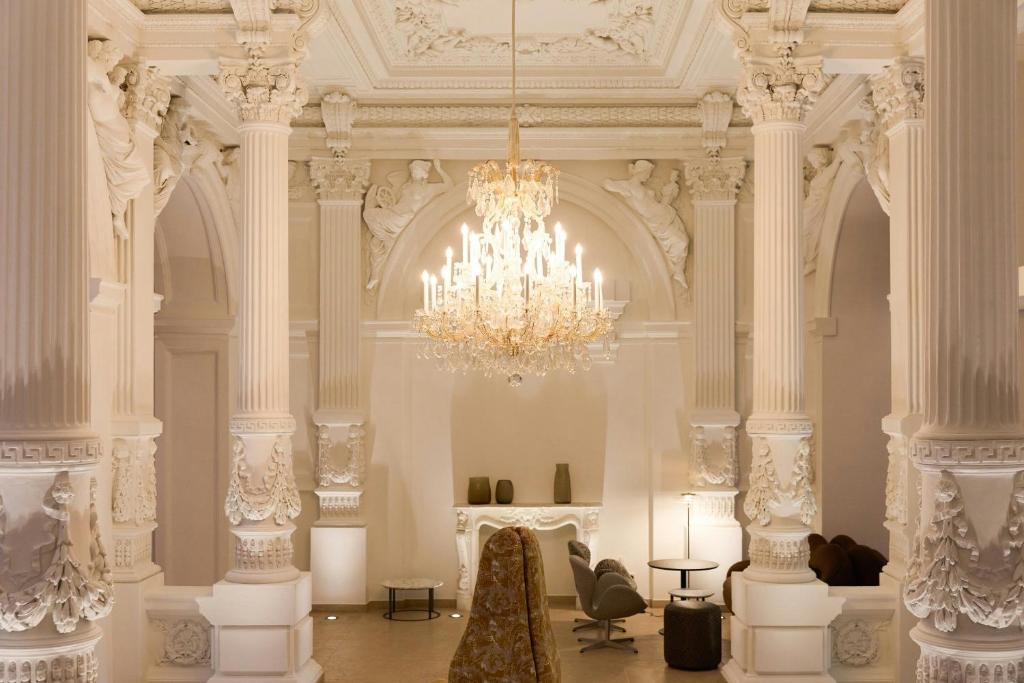 a large white room with a chandelier and columns at The Cloud One Wien-Staatsoper in Vienna