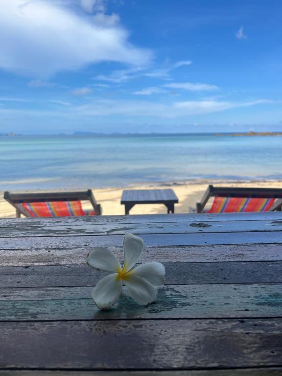a white flower sitting on a wooden table near the beach at Benjamin's Hut in Srithanu