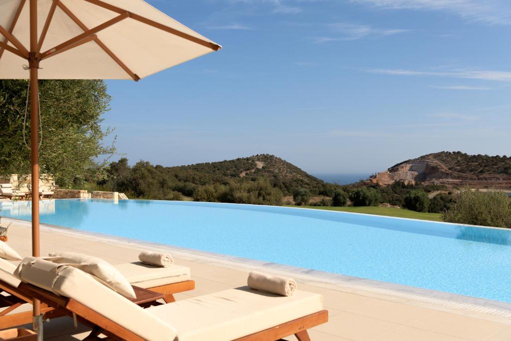 ein Pool mit Stühlen und Sonnenschirm und ein Swimmingpool in der Unterkunft Crete Golf Club Hotel in Hersonissos