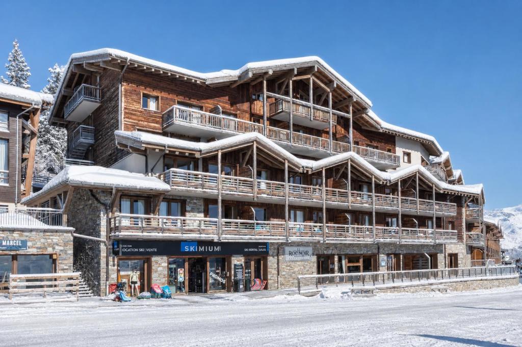 a large wooden building on a snowy street at Residence Le Roc Noir by Alpapart in La Rosière